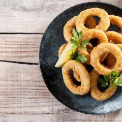 Calamares rebozados crujientes, dorados y listos para disfrutar, acompañados de limón y perejil.