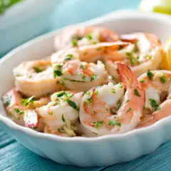 Deliciosos langostinos a la plancha, servidos en un cuenco blanco con perejil picado y una rodaja de limón.