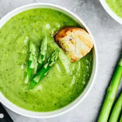 Crema de espárragos verde vibrante, decorada con espárragos frescos y un trozo de pan tostado.