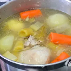 Olla con caldo de pollo casero hirviendo, con trozos de zanahoria, puerro, cebolla y pollo.