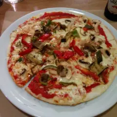 Pizza con masa de trigo sarraceno, cubierta con queso derretido, pimientos rojos y verdes, champiñones y berenjena.