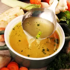 Sirviendo un reconfortante caldo de verduras recién hecho, rodeado de zanahorias, apio, puerro y ajo.