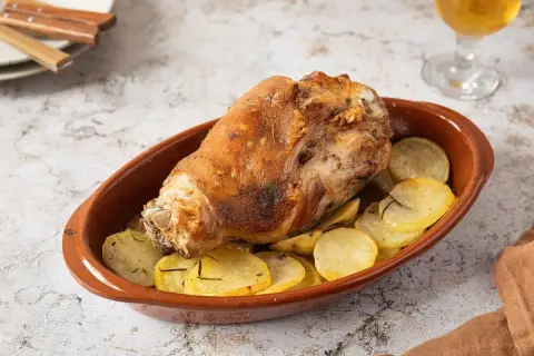 Codillo de cerdo asado, crujiente y dorado, servido en cazuela de barro con patatas panadera.