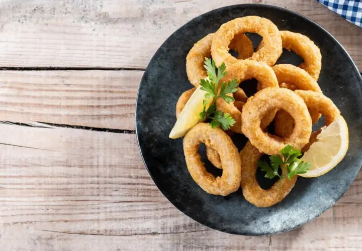 Calamares rebozados crujientes, dorados y listos para disfrutar, acompañados de limón y perejil.
