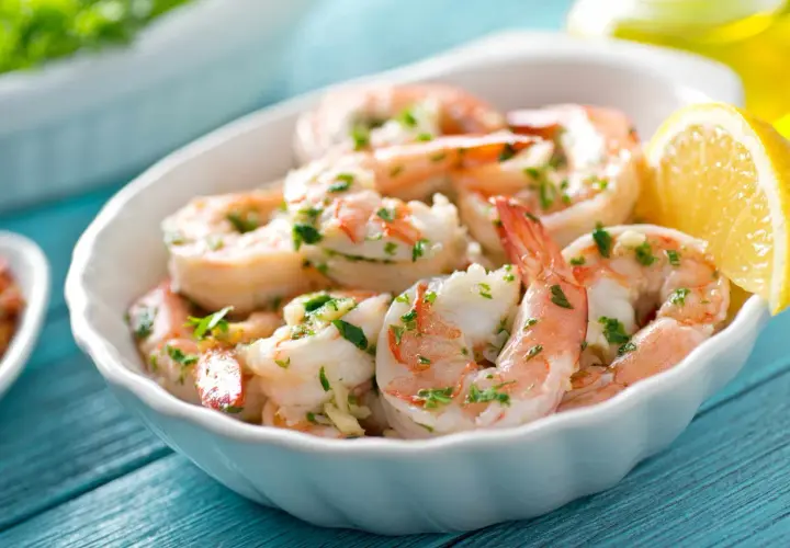 Deliciosos langostinos a la plancha, servidos en un cuenco blanco con perejil picado y una rodaja de limón.