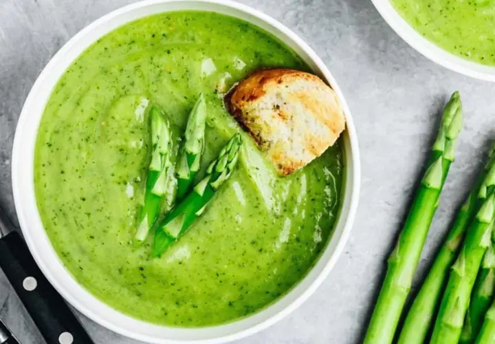 Crema de espárragos verde vibrante, decorada con espárragos frescos y un trozo de pan tostado.