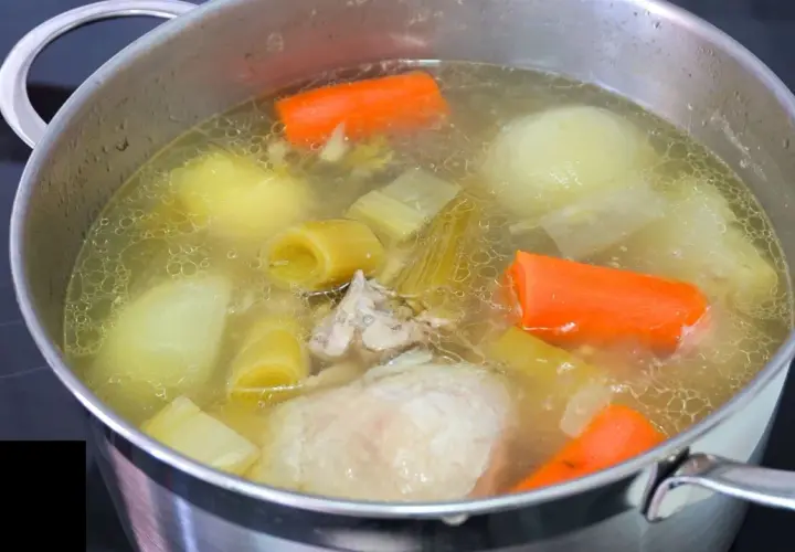 Olla con caldo de pollo casero hirviendo, con trozos de zanahoria, puerro, cebolla y pollo.