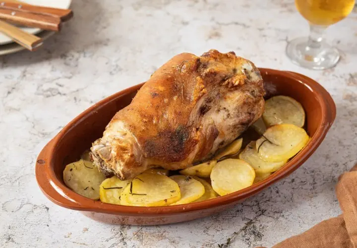 Codillo de cerdo asado, crujiente y dorado, servido en cazuela de barro con patatas panadera.