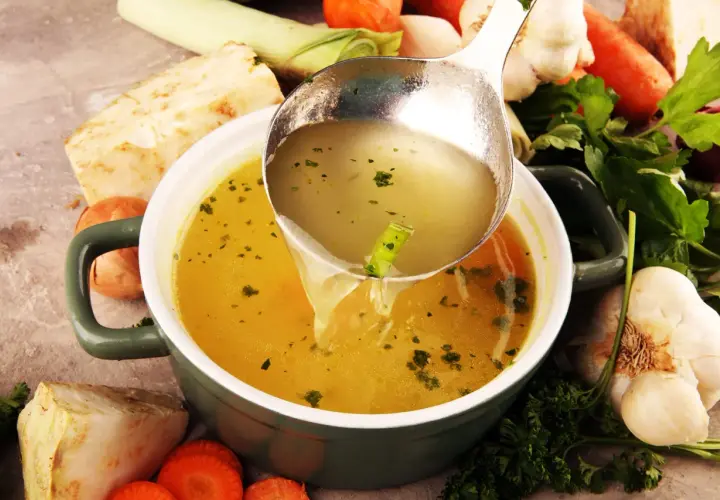 Sirviendo un reconfortante caldo de verduras recién hecho, rodeado de zanahorias, apio, puerro y ajo.