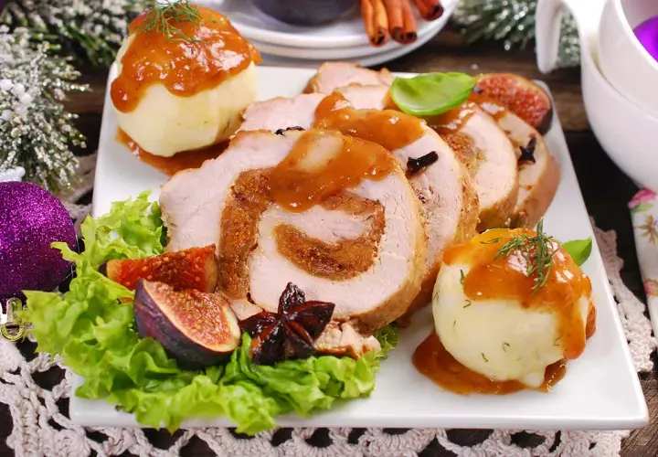 Rollo de cerdo relleno, servido con puré de patatas y salsa. Un plato festivo que recuerda a un cerdo trufero, decorado con higos y adornos navideños.
