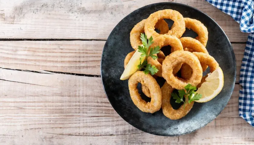 Calamares rebozados crujientes, dorados y listos para disfrutar, acompañados de limón y perejil.