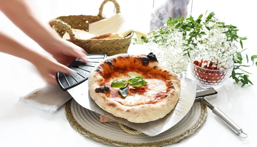 Manos estirando masa de pizza. Pizza recién horneada con albahaca y tomates secos, lista para servir.