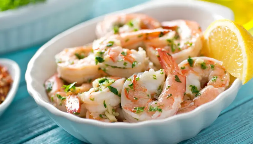 Deliciosos langostinos a la plancha, servidos en un cuenco blanco con perejil picado y una rodaja de limón.
