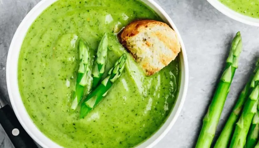 Crema de espárragos verde vibrante, decorada con espárragos frescos y un trozo de pan tostado.
