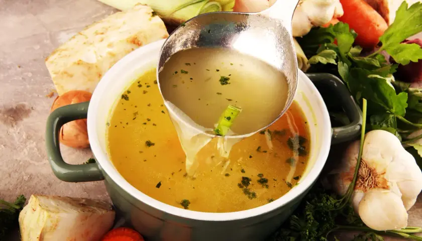 Sirviendo un reconfortante caldo de verduras recién hecho, rodeado de zanahorias, apio, puerro y ajo.