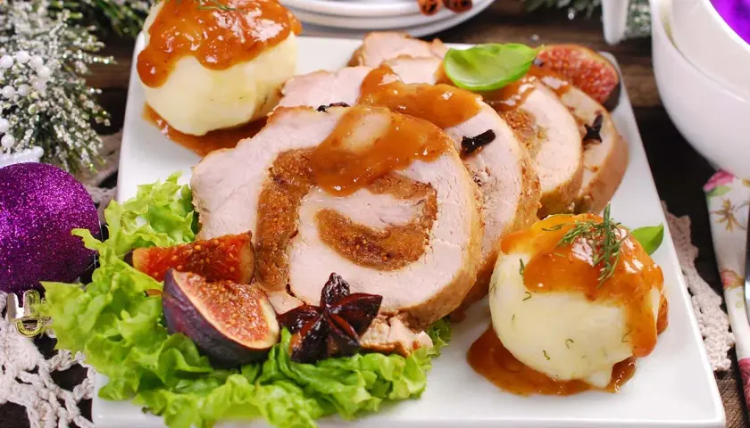 Rollo de cerdo relleno, servido con puré de patatas y salsa. Un plato festivo que recuerda a un cerdo trufero, decorado con higos y adornos navideños.