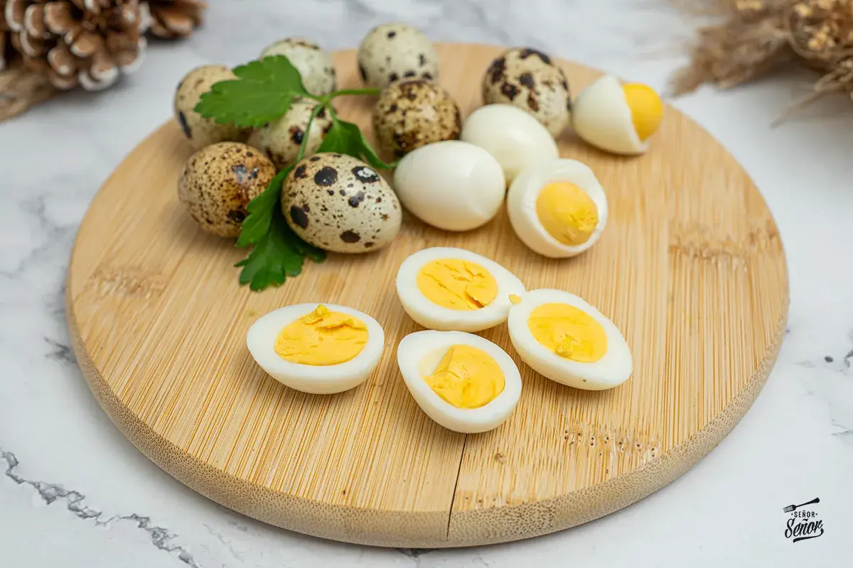 Huevos de codorniz cocidos y cortados por la mitad, mostrando sus yemas amarillas. Unos pocos huevos enteros y ramitas de perejil completan la escena.