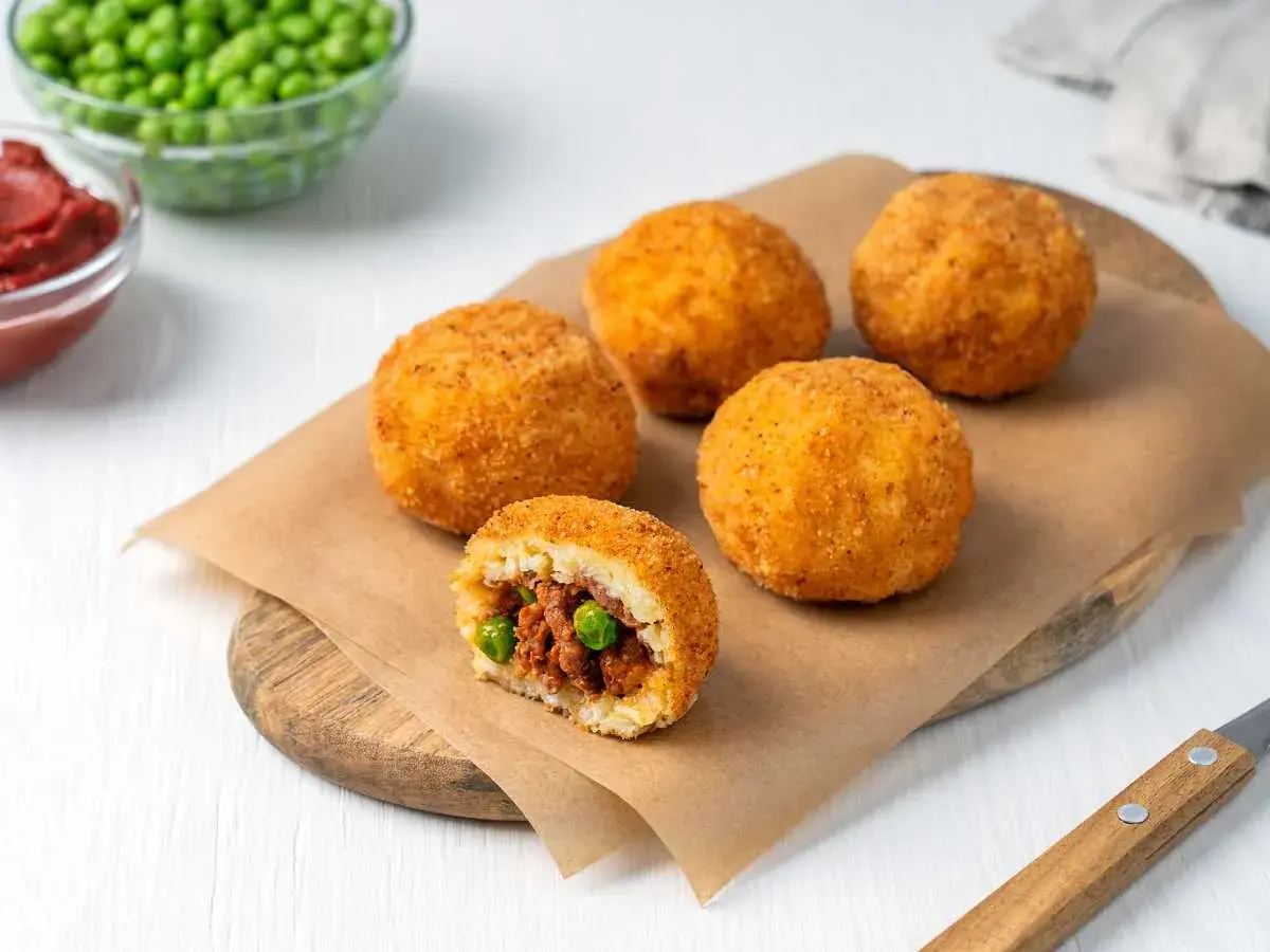 Arancini dorados y crujientes, uno cortado revela un relleno de carne y guisantes. ¡Una deliciosa receta arancini lista para disfrutar!