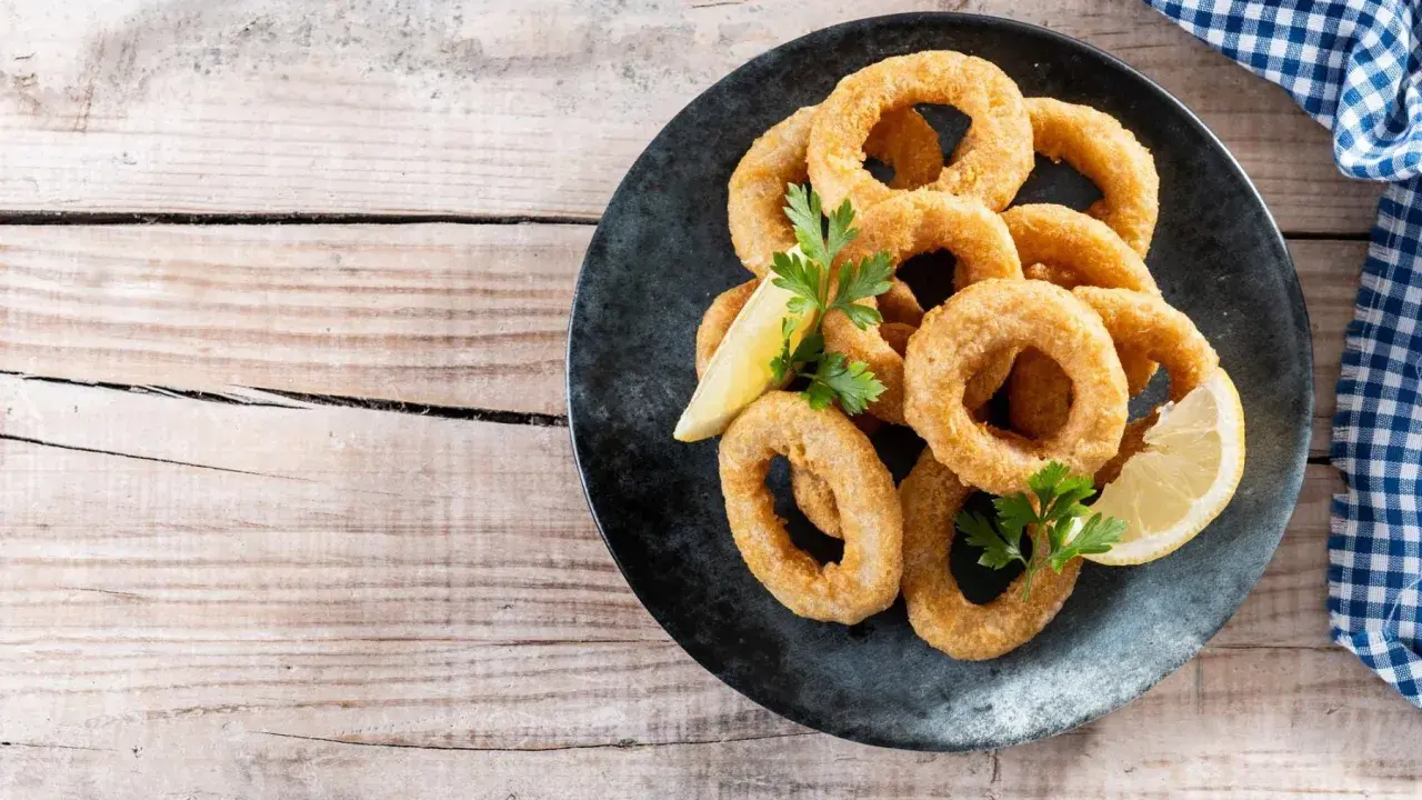 Calamares rebozados crujientes, dorados y listos para disfrutar, acompañados de limón y perejil.
