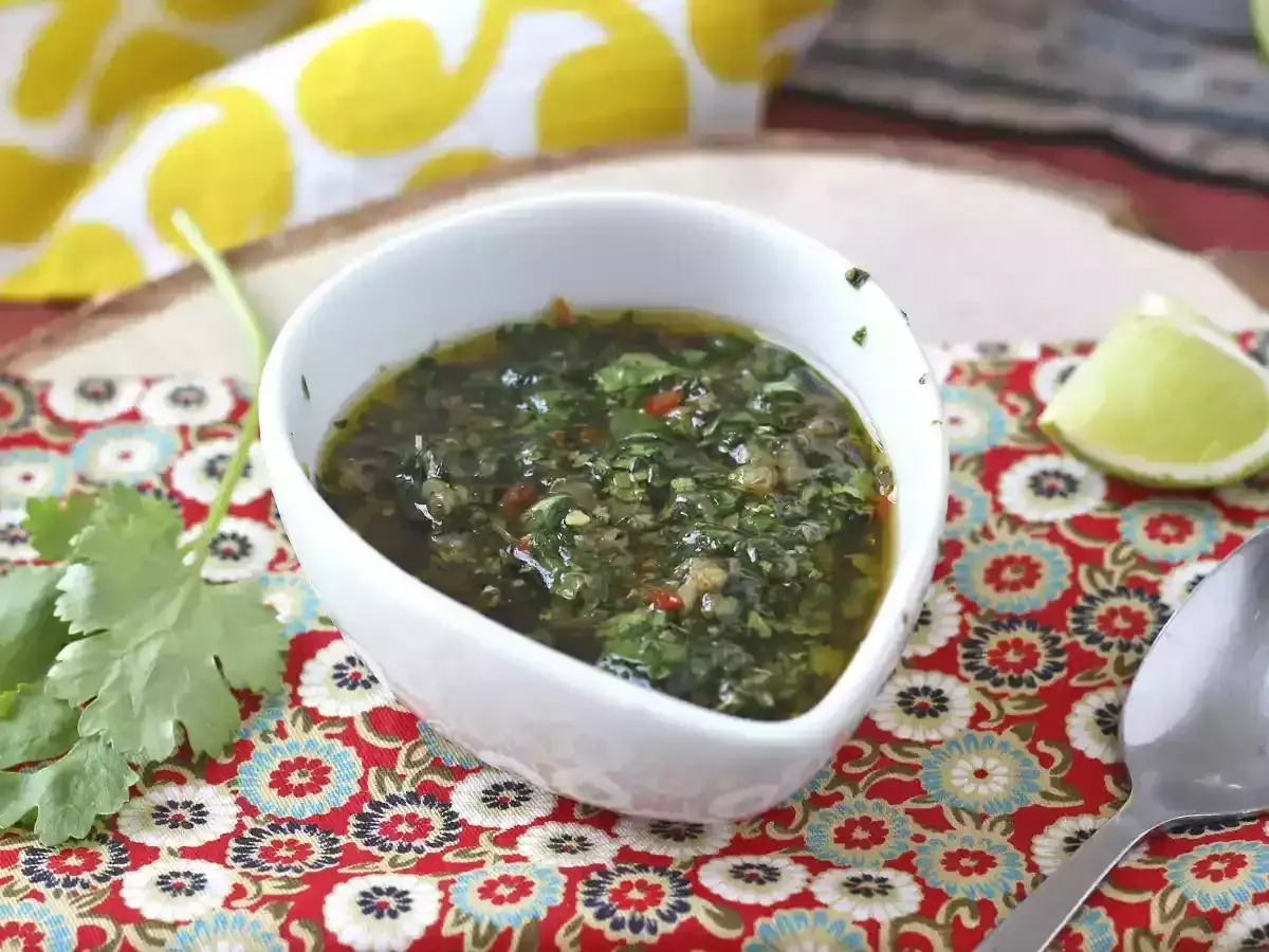 Un tazón blanco con una deliciosa **receta de chimichurri** casera, adornado con cilantro fresco y una rodaja de limón.