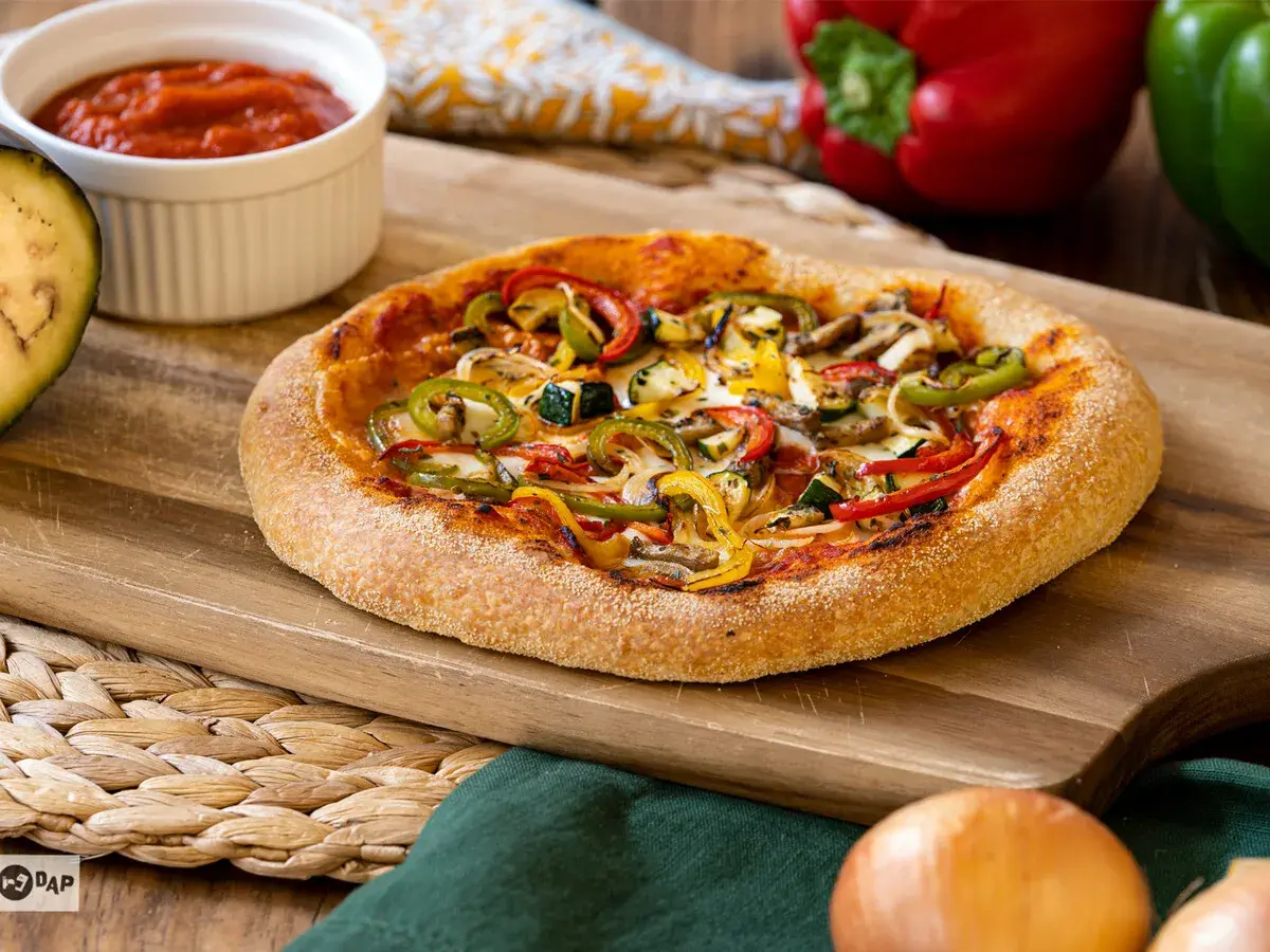 Pizza vegana con pimientos, calabacín y champiñones sobre tabla de madera. Salsa de tomate y berenjena al lado.