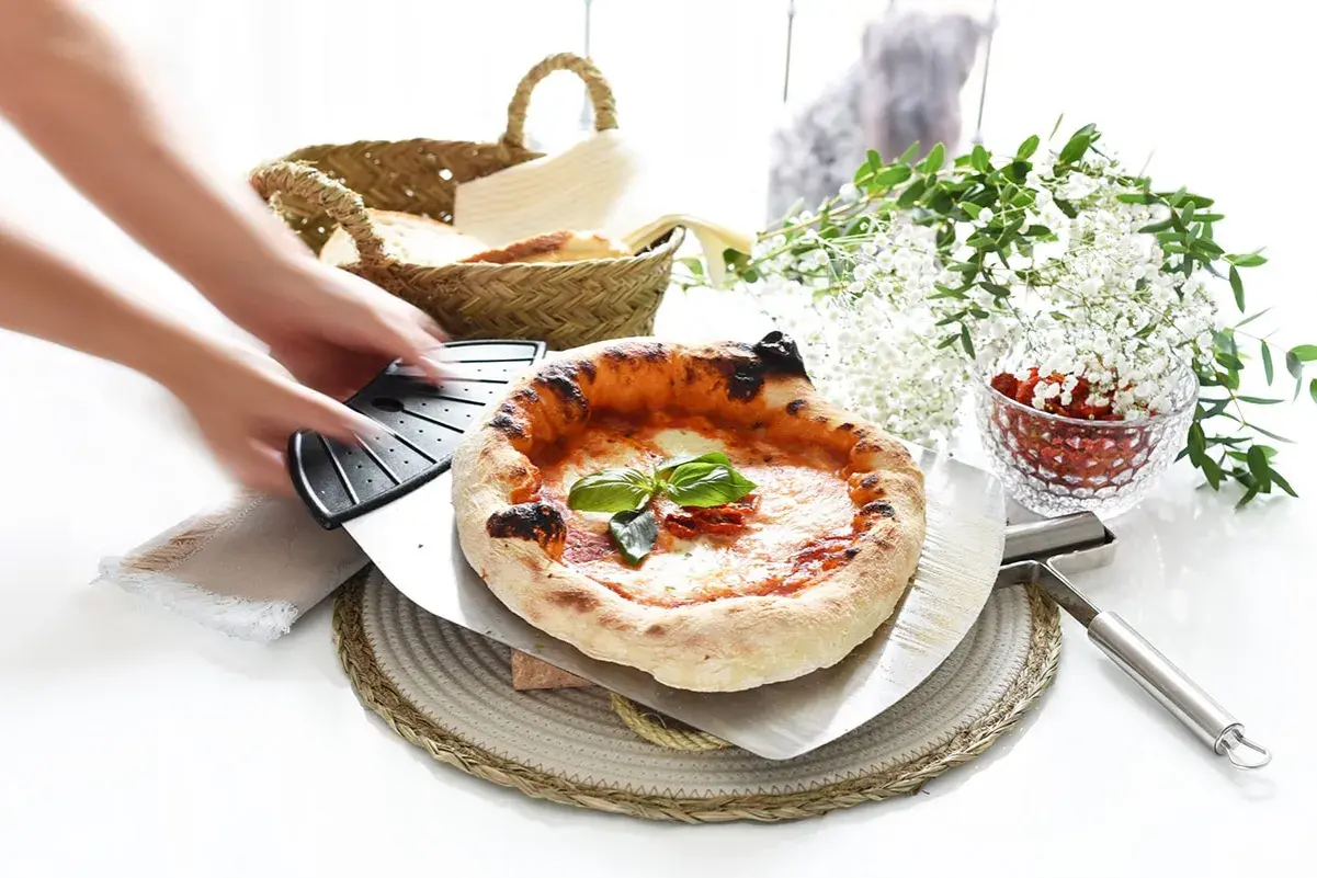 Manos estirando masa de pizza. Pizza recién horneada con albahaca y tomates secos, lista para servir.