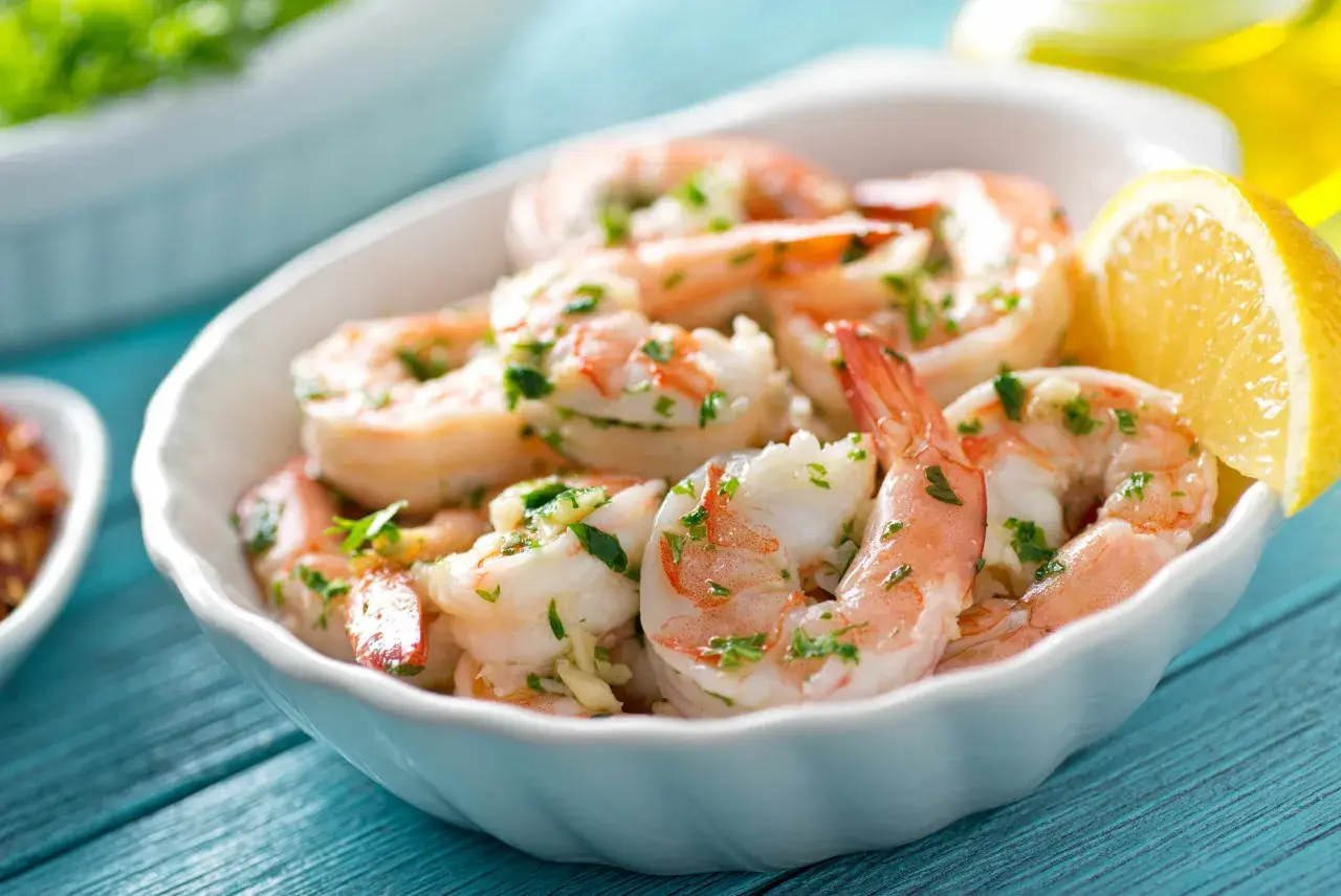 Deliciosos langostinos a la plancha, servidos en un cuenco blanco con perejil picado y una rodaja de limón.
