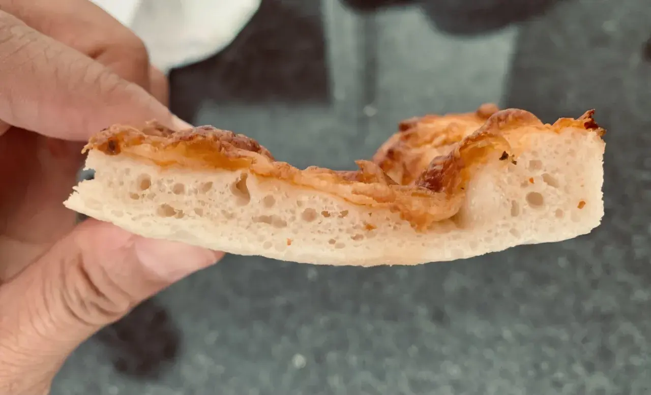 Rebanada de pizza con burbujas perfectas en la masa, dorada y crujiente.