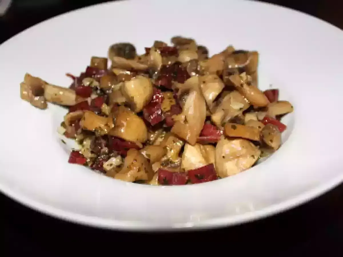 Champiñones al ajillo con jamón, un plato sabroso y aromático, servido en un plato blanco.