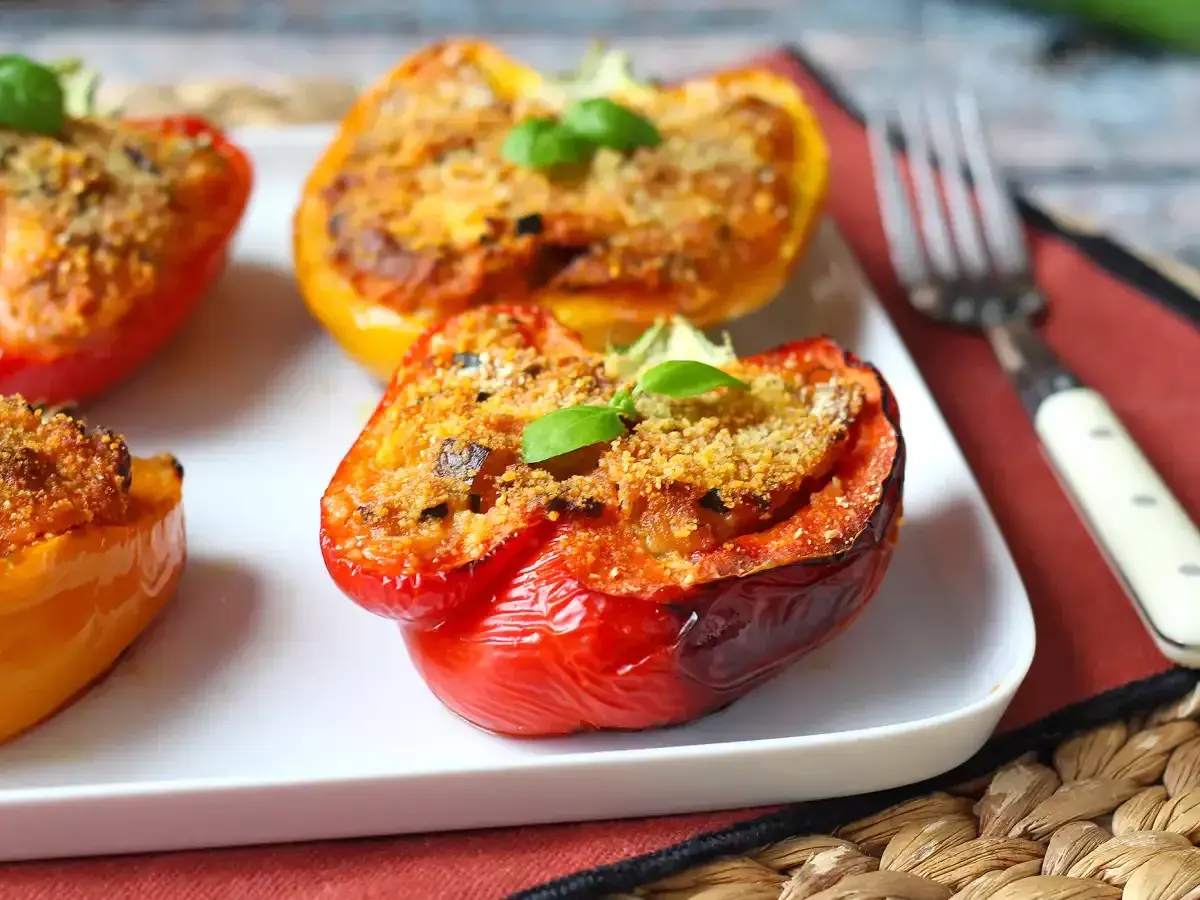 Pimientos rellenos vegetarianos, dorados y gratinados, con una hoja de albahaca fresca coronando cada uno.