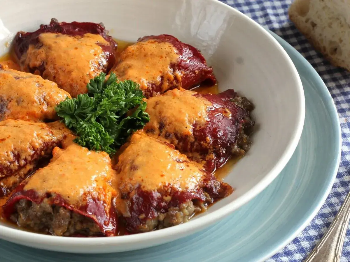 Pimientos rellenos de carne, cubiertos con una cremosa salsa naranja y adornados con perejil fresco.