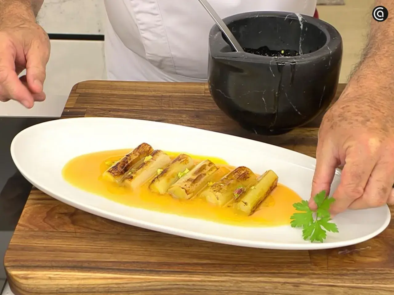 Puerros a la plancha, dorados y tiernos, servidos en una salsa anaranjada y decorados con perejil fresco.