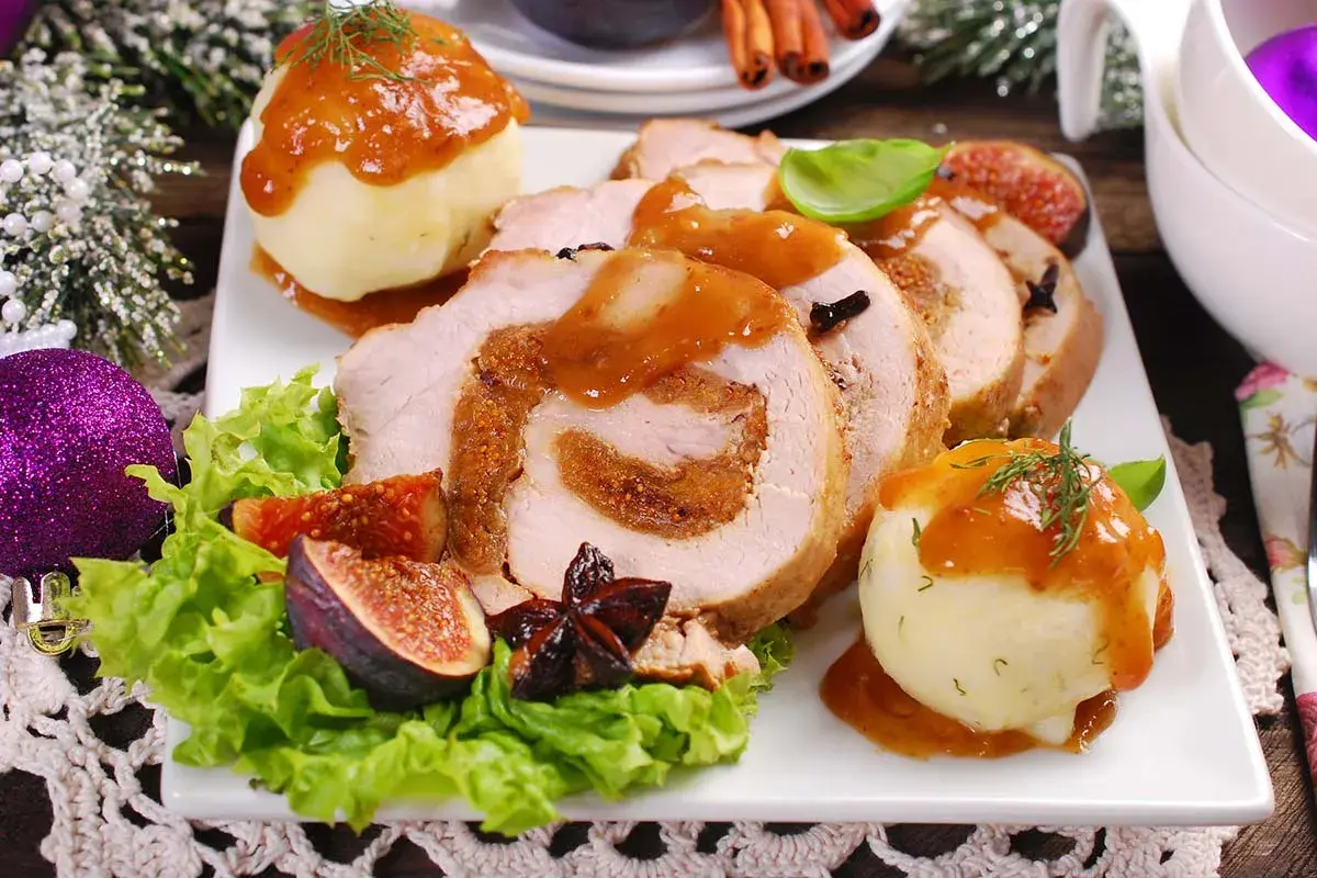 Rollo de cerdo relleno, servido con puré de patatas y salsa. Un plato festivo que recuerda a un cerdo trufero, decorado con higos y adornos navideños.