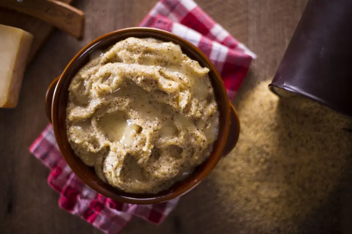 Polenta taragna cremosa servida en cuenco de barro, con queso y maíz esparcido alrededor.