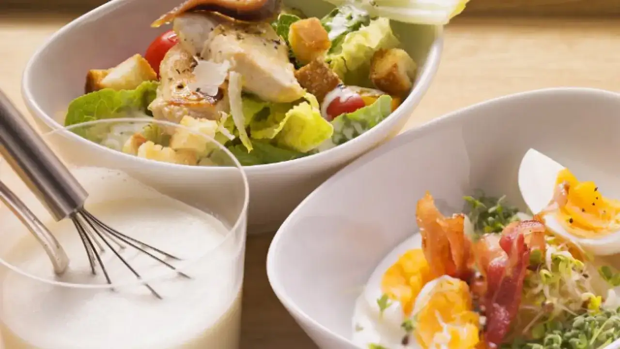 Ensalada César con pollo, crutones y un vaso con batidor y salsa cremosa, quizás una salsa César vegana.