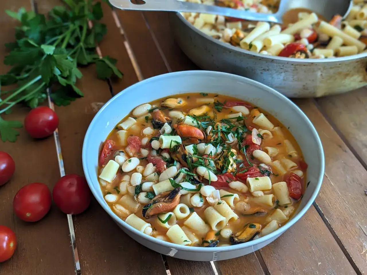 Un reconfortante plato de pasta e fagioli con mejillones, tomates y albahaca fresca, servido en un cuenco blanco.