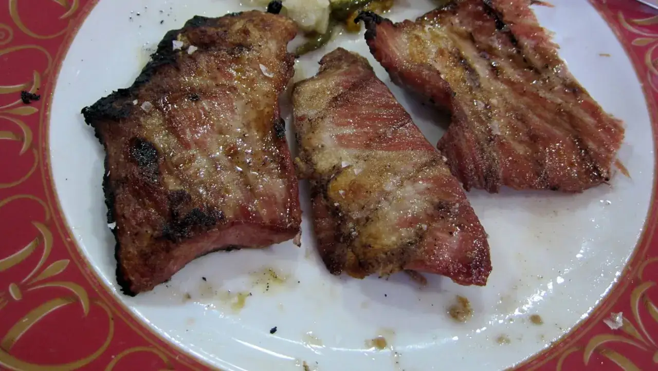 Tres trozos de secreto de cerdo a la parrilla, jugosos y con sal gruesa, servidos en un plato blanco con borde rojo.