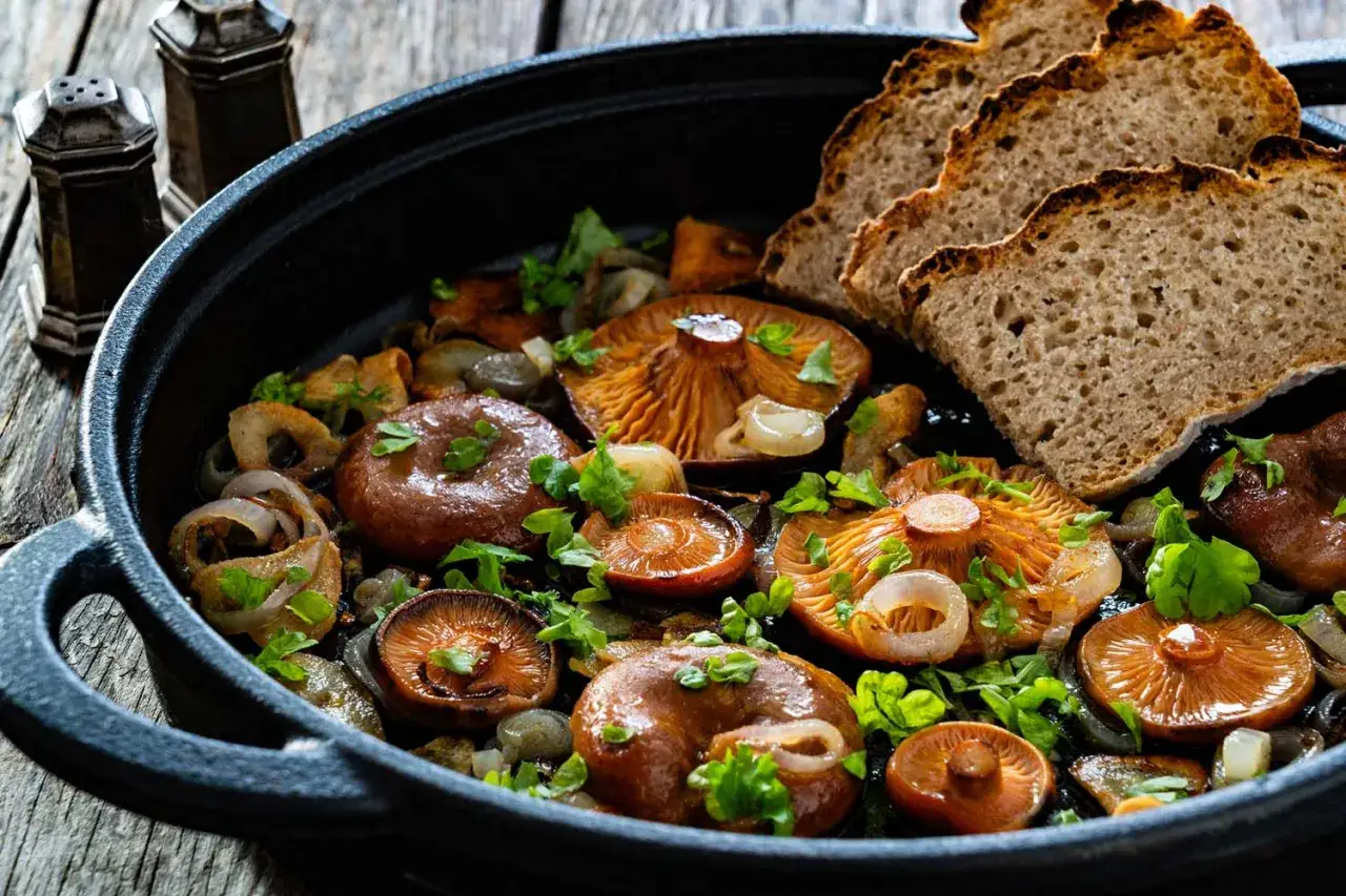 Niscalos salteados con cebolla y perejil, servidos en sartén de hierro fundido con rebanadas de pan rústico. ¡Una de las mejores niscalos recetas!