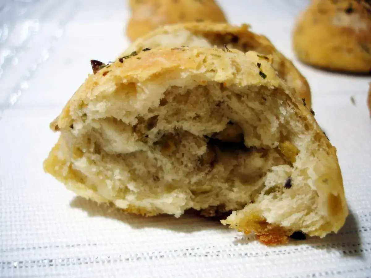 Pan rústico de pan de aceitunas, con miga esponjosa y trozos de aceitunas verdes y negras incrustados.