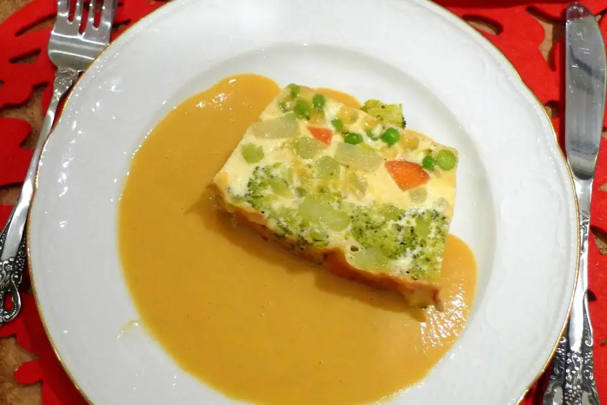 Porci&oacute;n de pastel de verduras con br&oacute;coli, zanahoria y guisantes, servida con una cremosa salsa.
