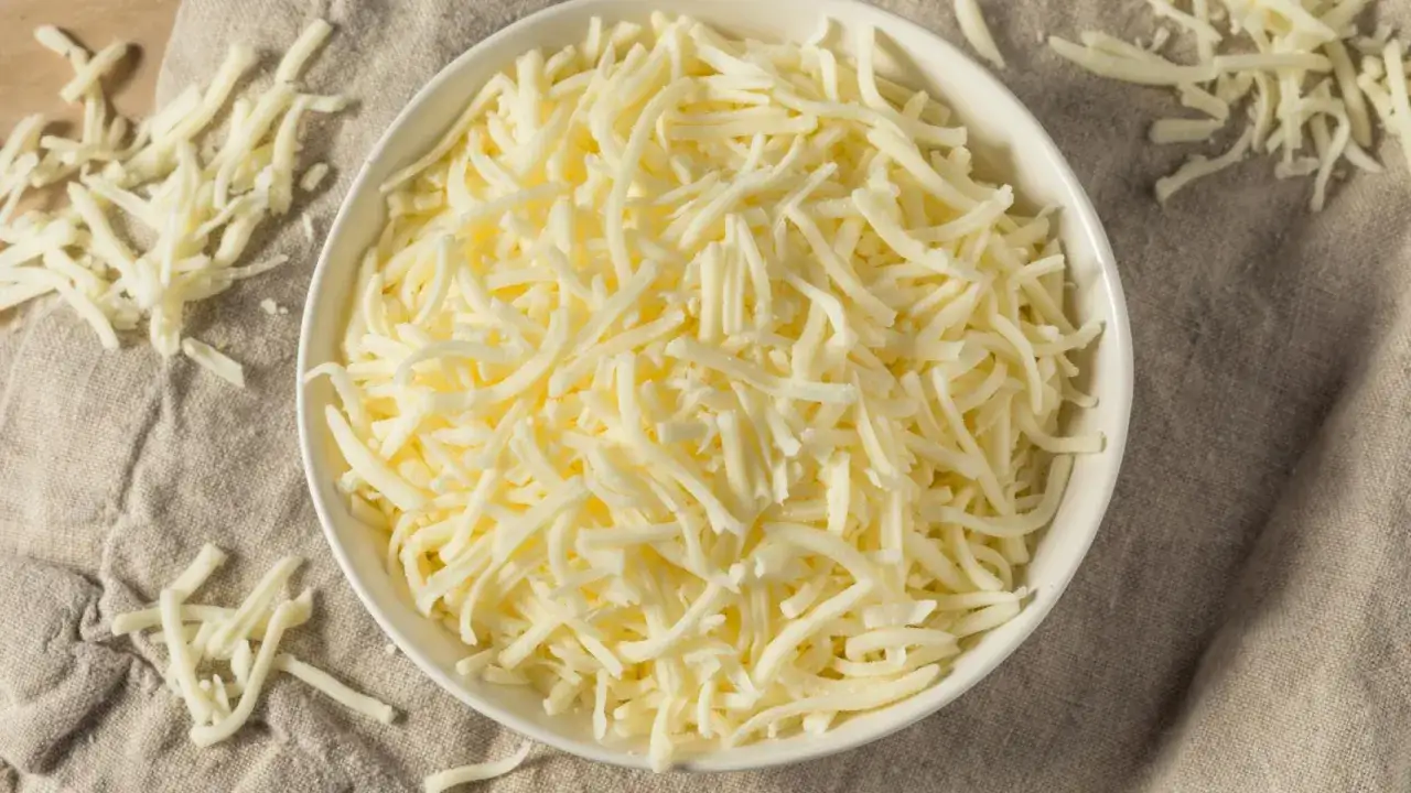 Un bol blanco lleno de queso mozzarella rallado, la mejor mozzarella para pizza, sobre una tela r&uacute;stica.