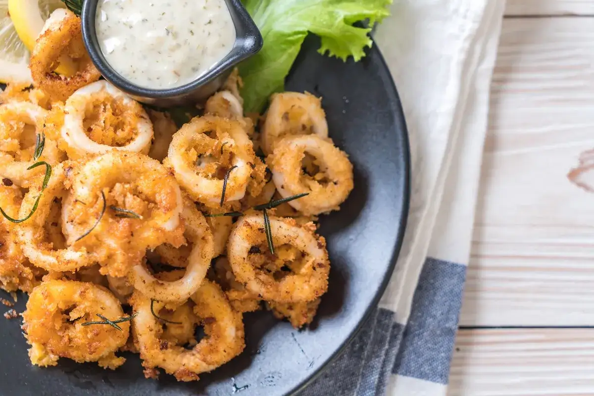 Calamares rebozados crujientes, dorados y servidos con una salsa cremosa y limón.