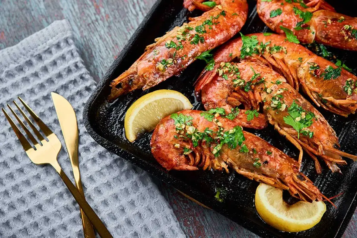 Deliciosos langostinos a la plancha, dorados y jugosos, servidos con rodajas de limón y perejil fresco. Un manjar listo para disfrutar.