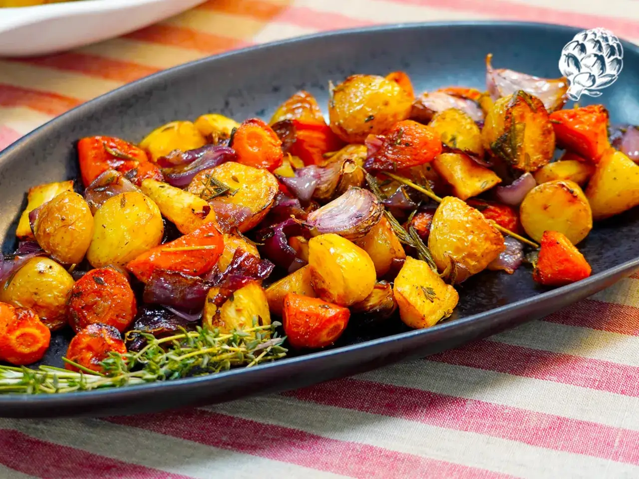 Plato de guarniciones de verduras asadas: patatas, zanahorias y cebolla morada, con hierbas frescas.