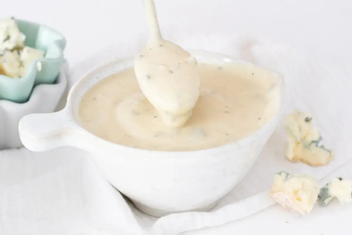 Cremosa salsa gorgonzola servida en un cuenco blanco, con trozos de queso azul esparcidos alrededor.
