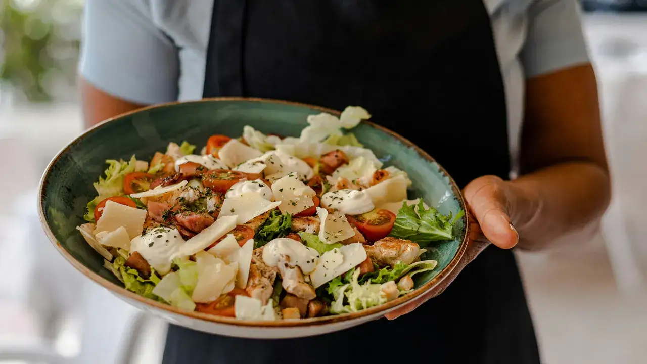 Una generosa ensalada César con pollo a la parrilla, tomates cherry, queso parmesano y aderezo cremoso, lista para servir.