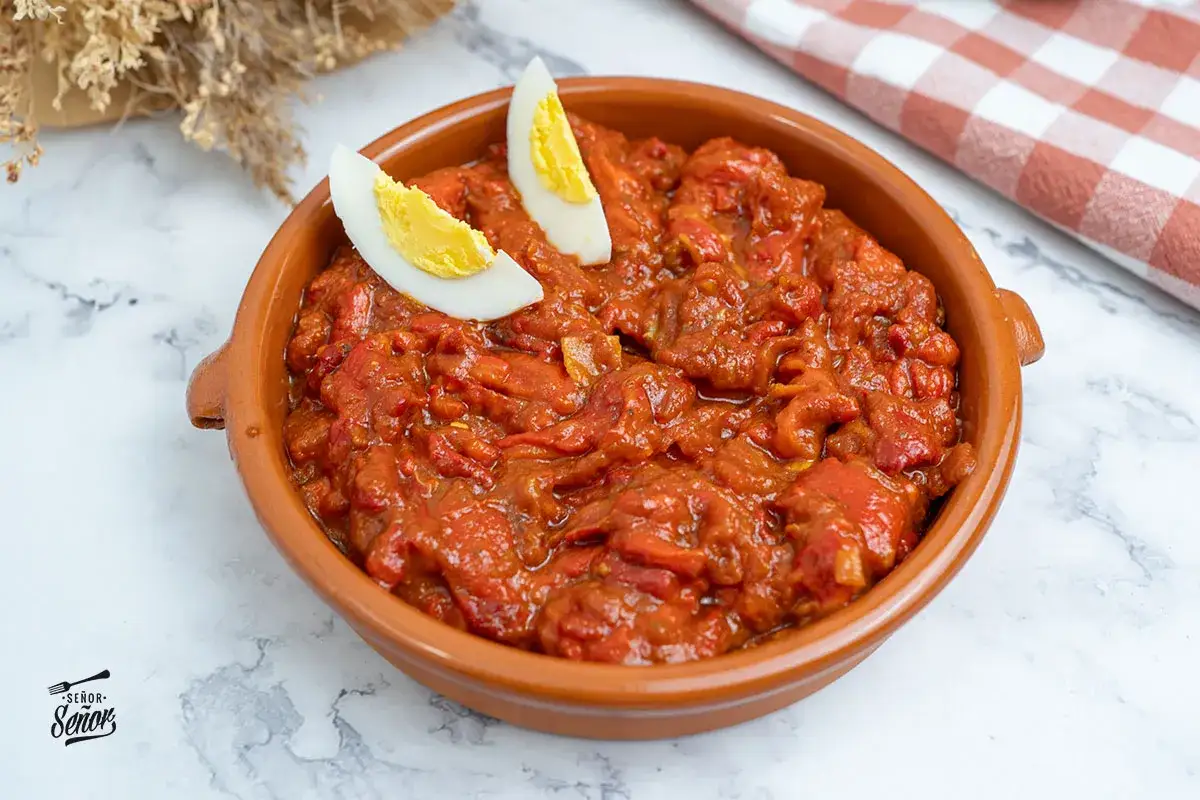 Un plato de asadillo manchego, guiso de pimientos asados y tomate, adornado con huevo duro.