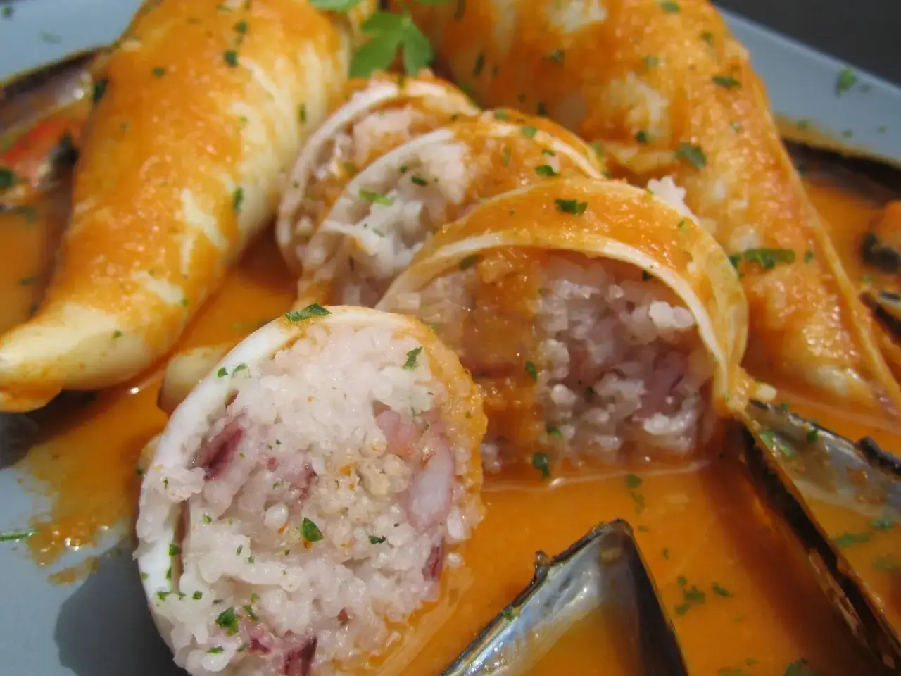 Calamares rellenos de arroz y mariscos, bañados en una salsa naranja y decorados con perejil.