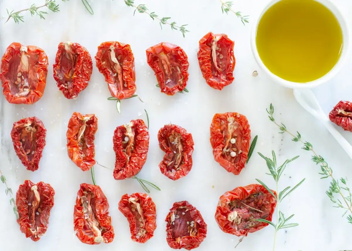 Tomates secos al horno, listos para usar en tus recetas. Aceite de oliva y hierbas frescas acompañan.