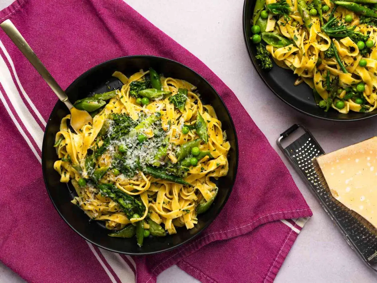 Un plato de pasta primavera con espárragos, guisantes y brócoli, espolvoreado con queso rallado.
